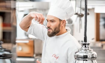 Chef tasting food with a spoon in a kitchen